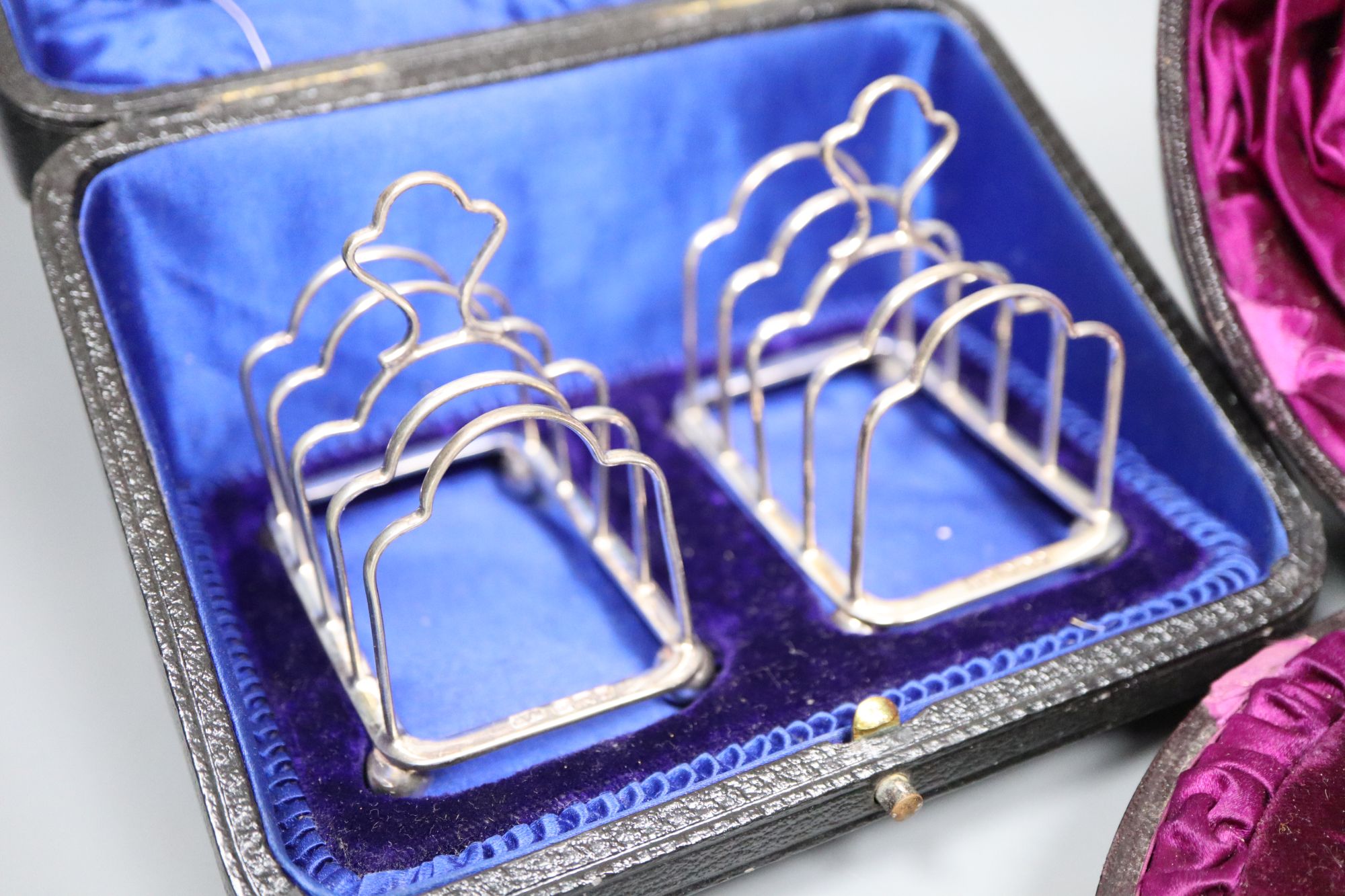 A Victorian silver three-piece condiment set, London, 1882, cased and a pair of small Edwardian silver toast racks, cased.